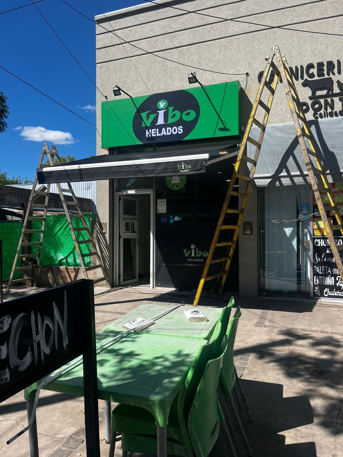 Una fachada verde de Vibe Helados con escaleras, asientos al aire libre y un letrero que dice