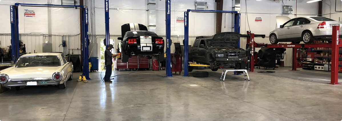 A row of cars are sitting on lifts in a garage. | Patterson Brothers Automotive