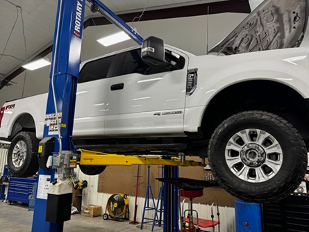 A white truck is sitting on a lift in a garage - Patterson Brothers Automotive