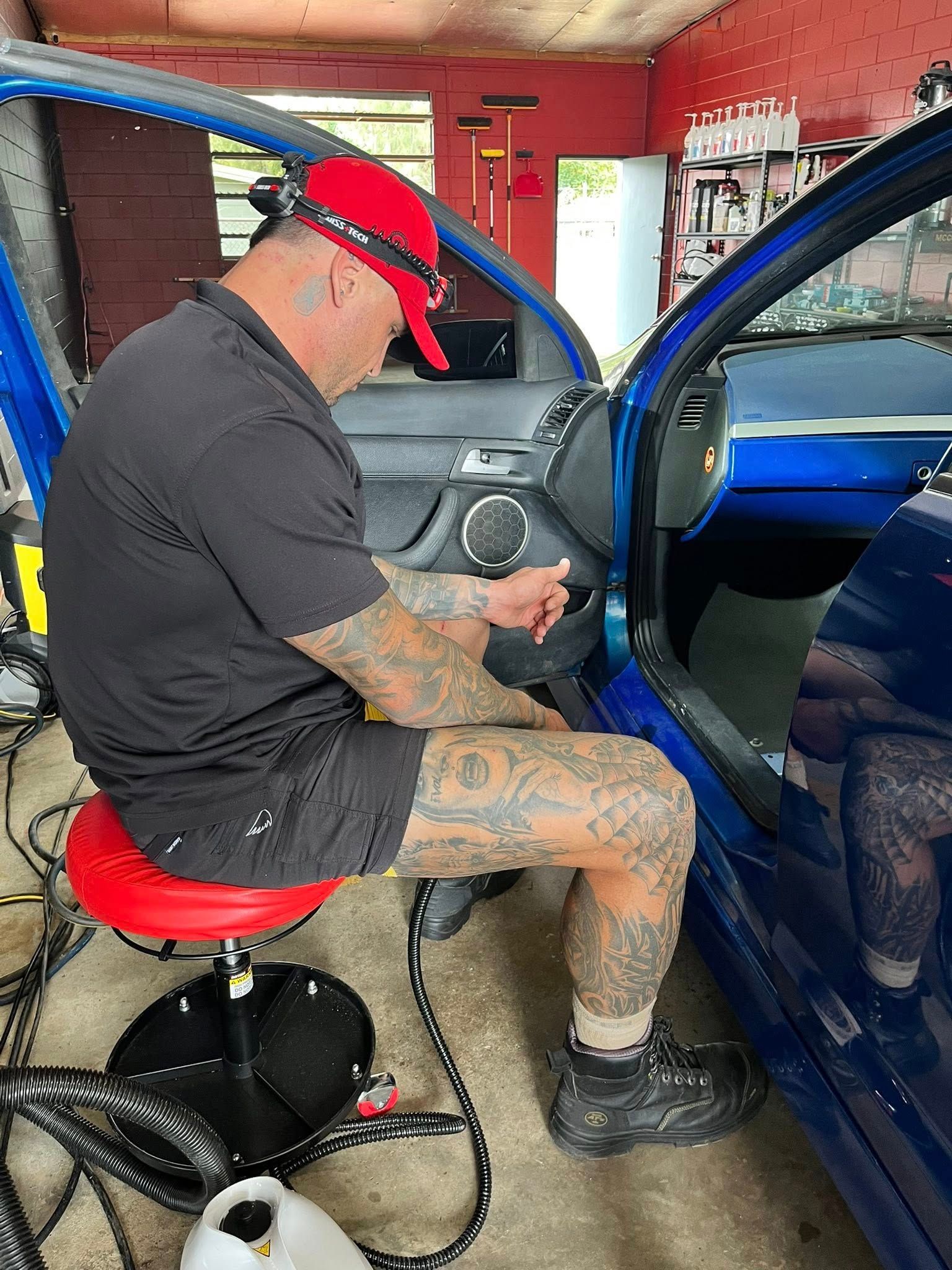 A Tattooed Person in a Red Cap Sits on a Red Rolling Stool — Mobile Club Cars Cairns in Tully, QLD