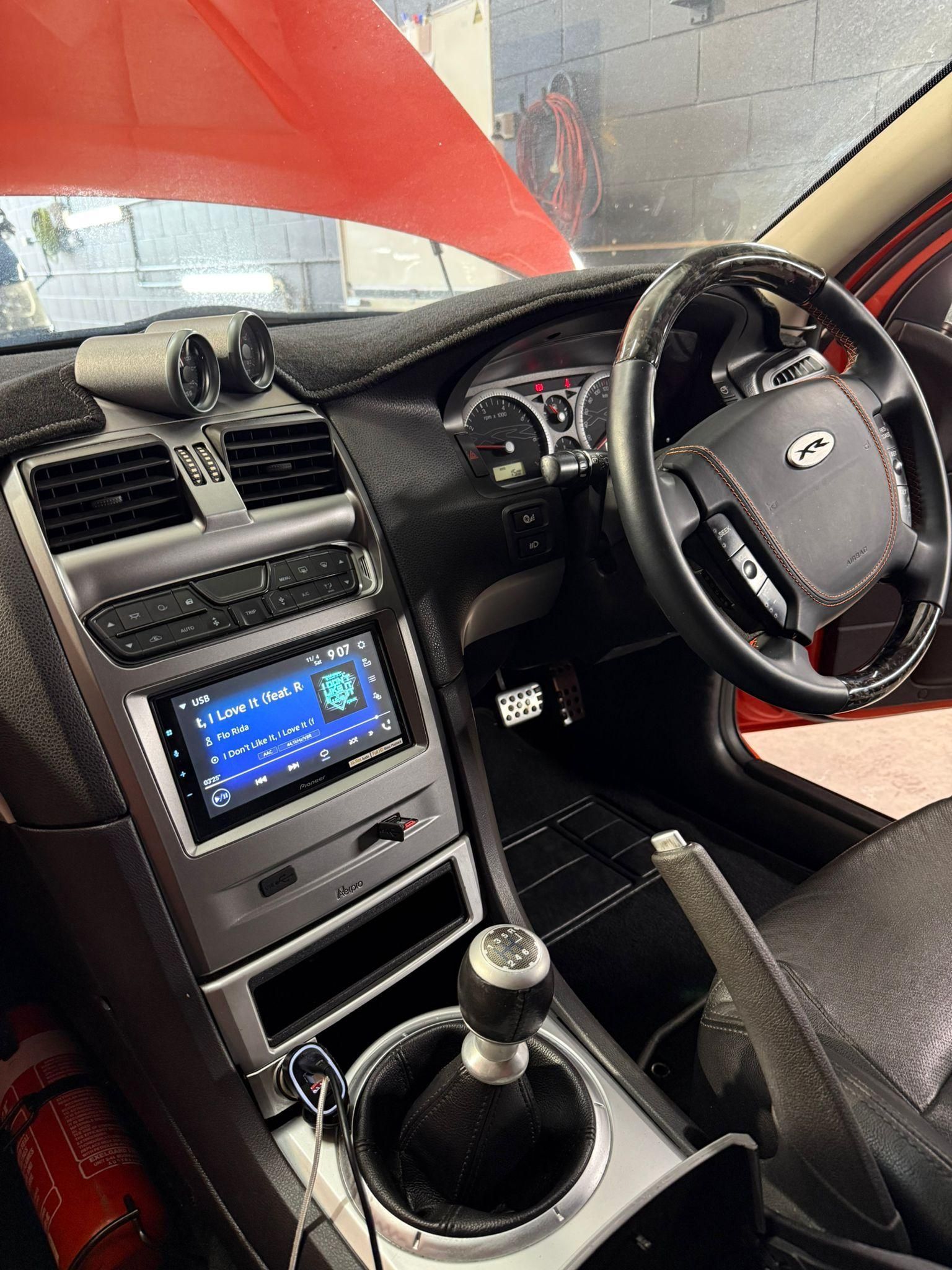 Car interior with manual gear shift, steering wheel, center display, and red hood visible through the windshield — Mobile Club Cars Cairns in Earlville, QLD