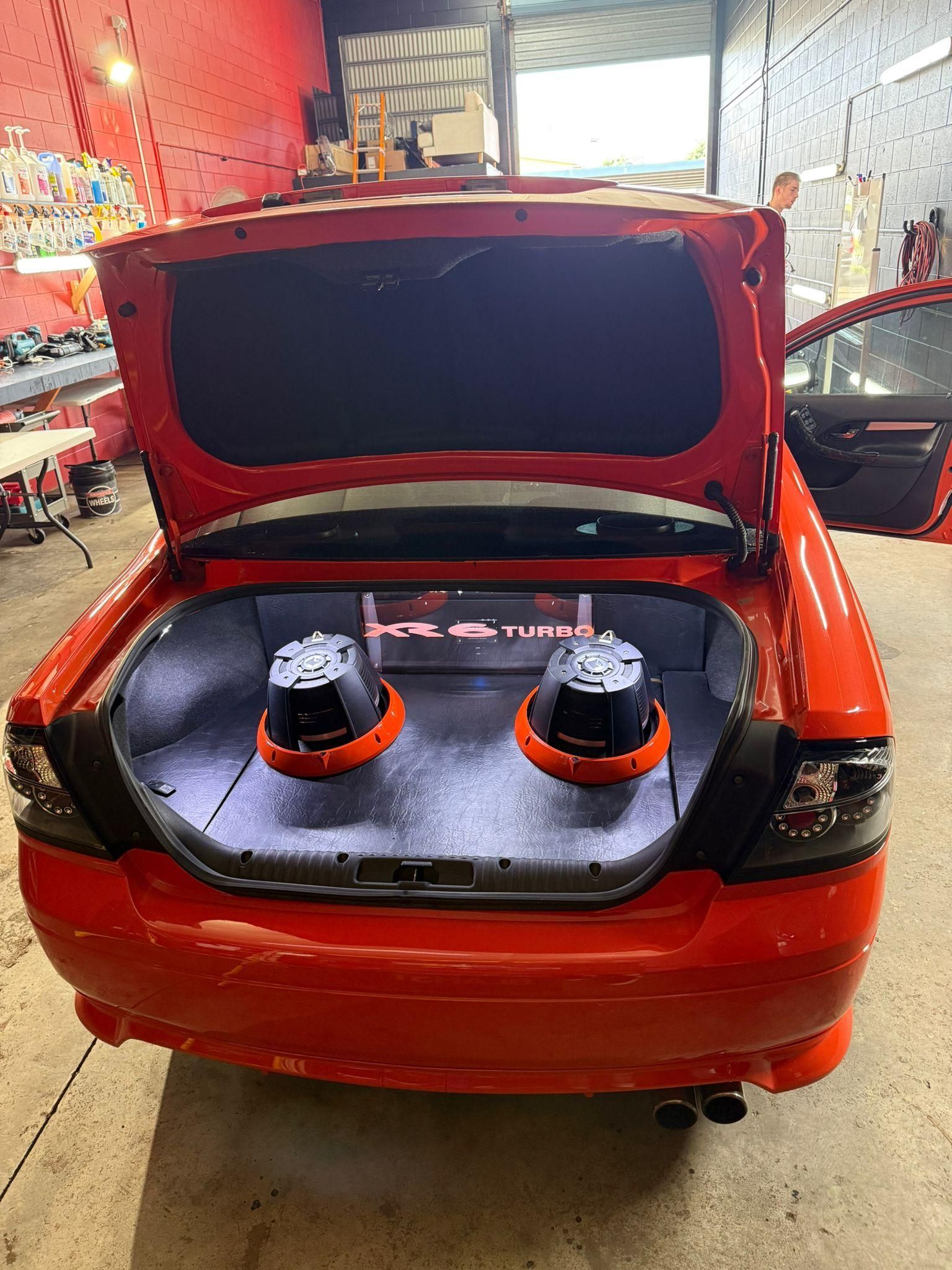 Red sedan in a garage with the trunk open, showing two subwoofers installed in the trunk — Mobile Club Cars Cairns in Earlville, QLD