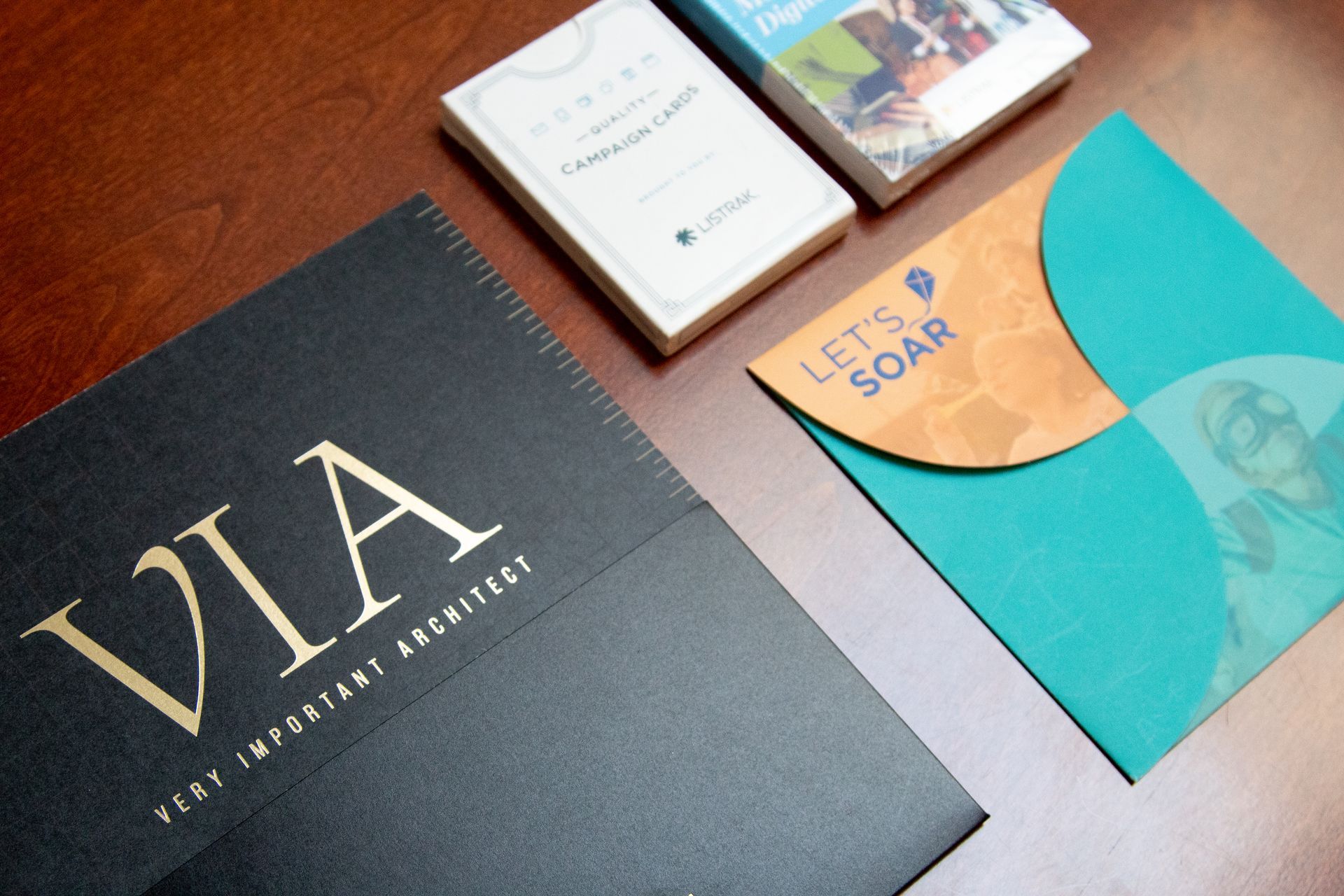 A book called via sits on a table next to a blue envelope that says let 's soar