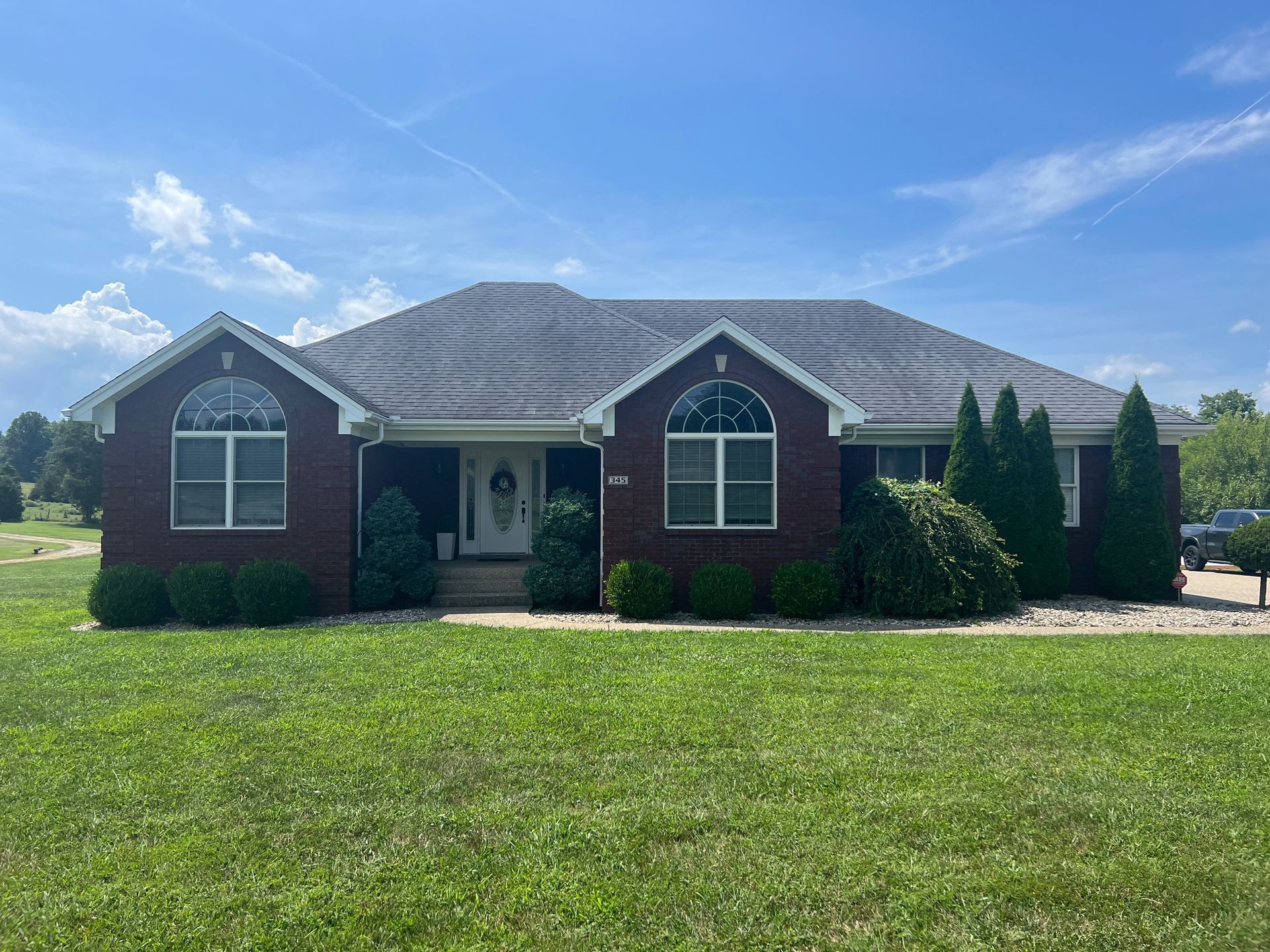 Brick ranch house with arched windows, dark roof, and green lawn on a sunny day.