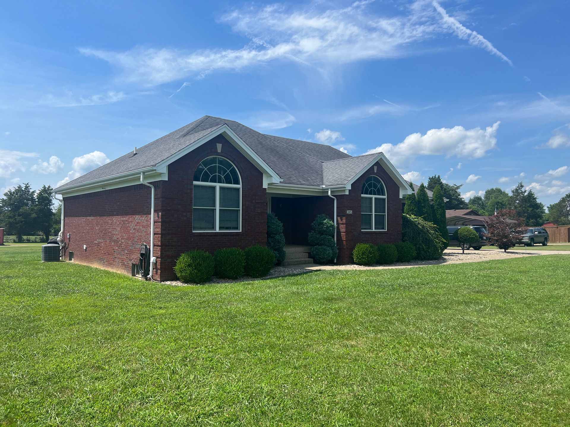 Brick house with a grassy lawn under a blue sky. Bushes frame the front windows.