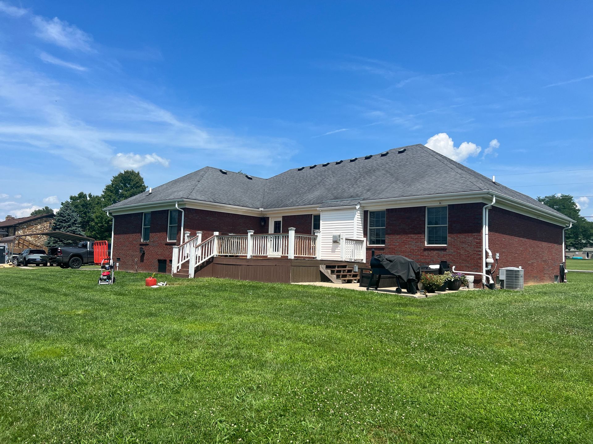 Brick house with a deck, white trim, and a green lawn under a blue sky.