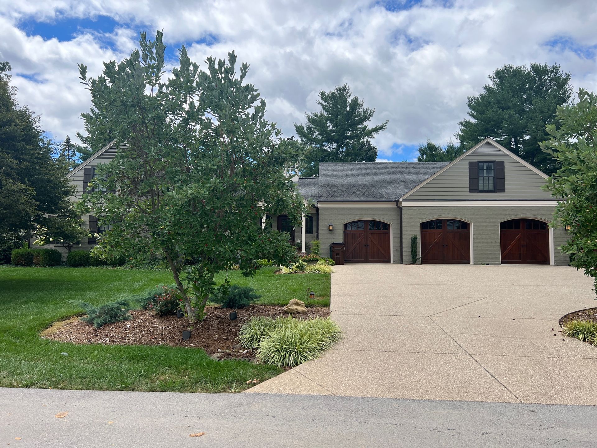 House with a gray roof and three brown garage doors. Driveway and landscaping in front.