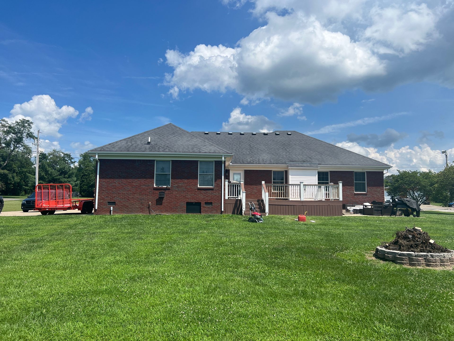 Brick house with a deck and green yard under a blue sky with fluffy clouds.