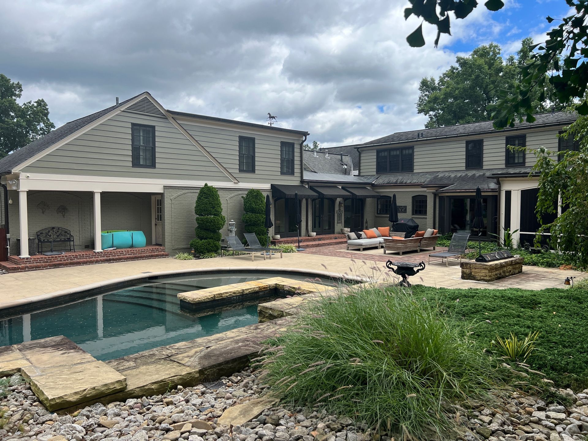 Backyard of a house with a pool. Smoke damage is visible on the roof and walls; cloudy sky.
