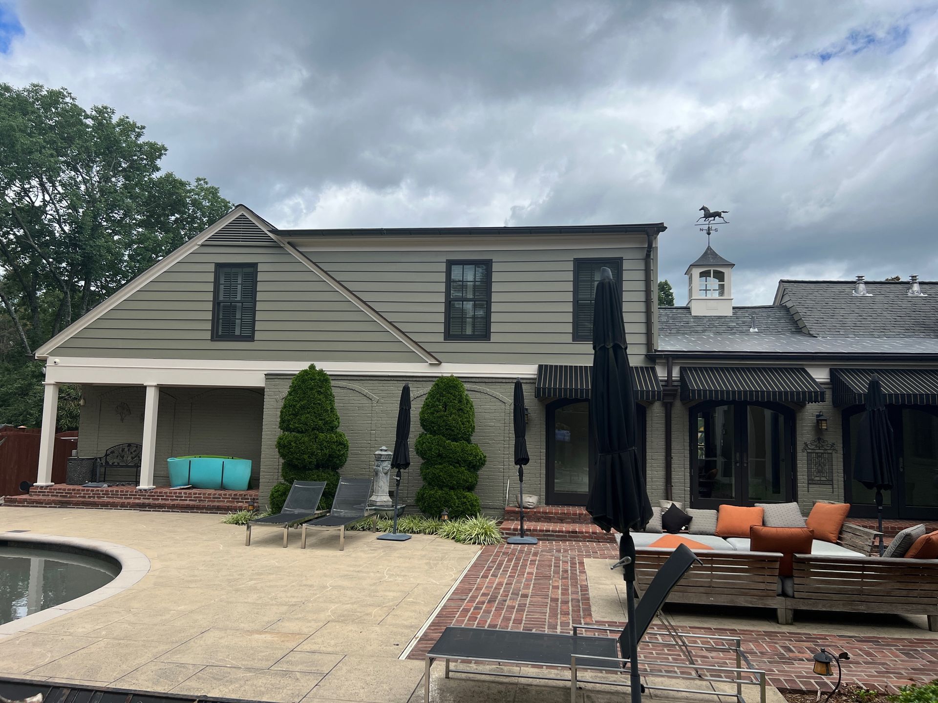 Backyard with pool, lounge area, and house; cloudy sky.