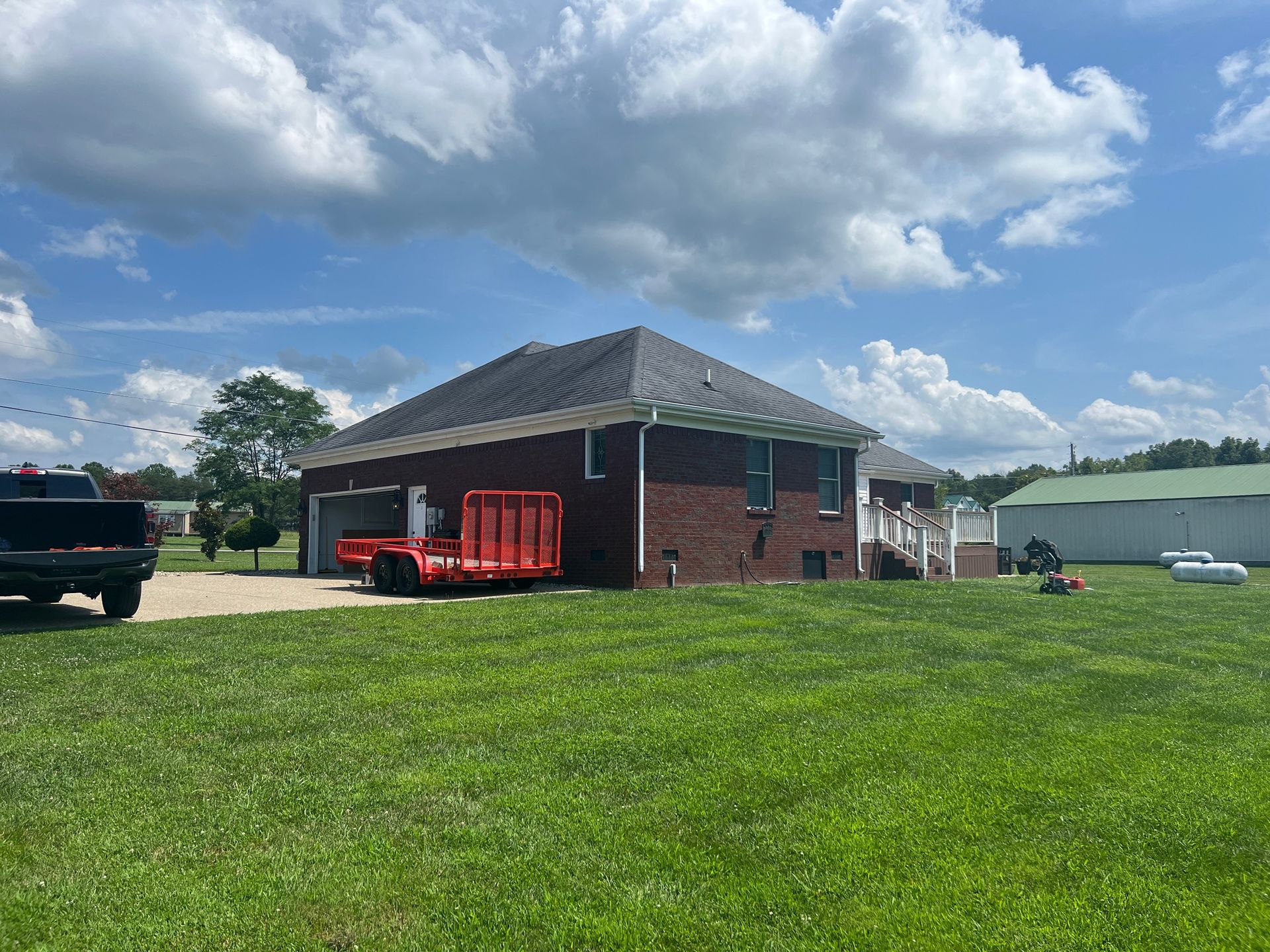 Brick house with green lawn, a trailer, and partly cloudy sky.
