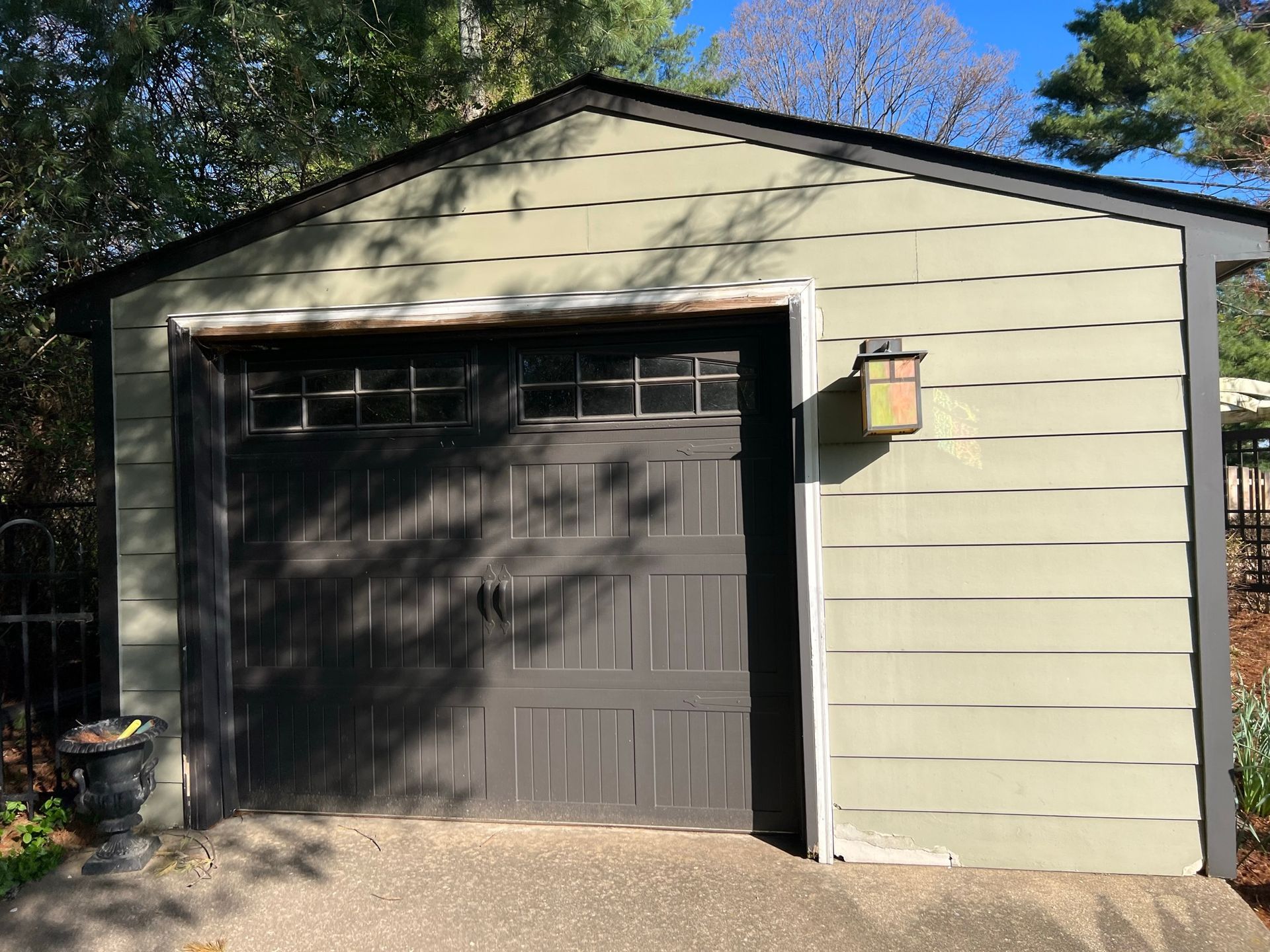 Green-sided garage with a black door, roof, and trim. A light fixture is attached to the right wall.