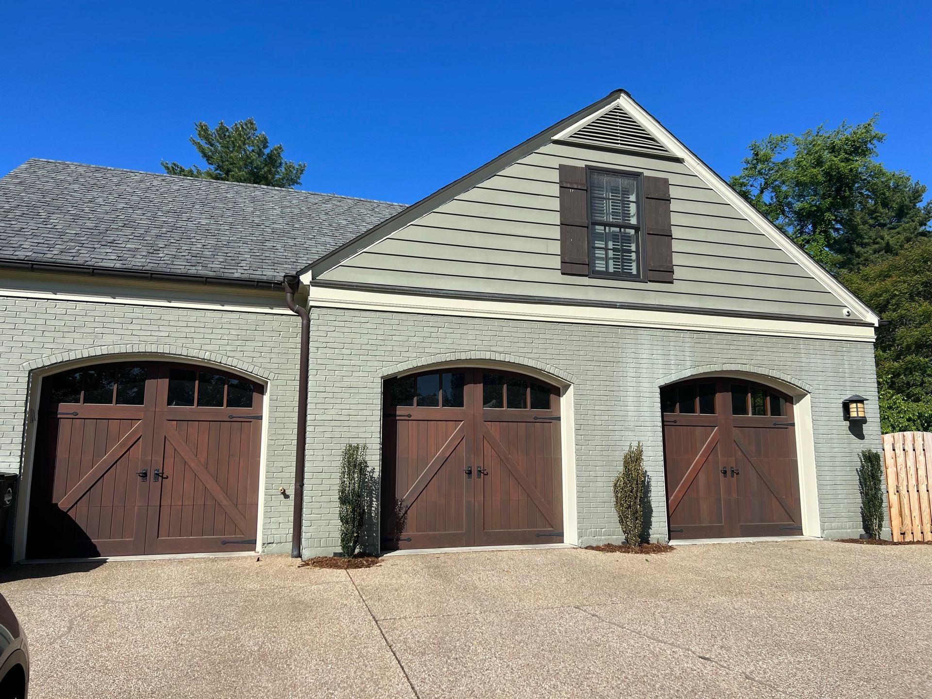 Three-bay garage with brown doors and grey siding, under a blue sky.