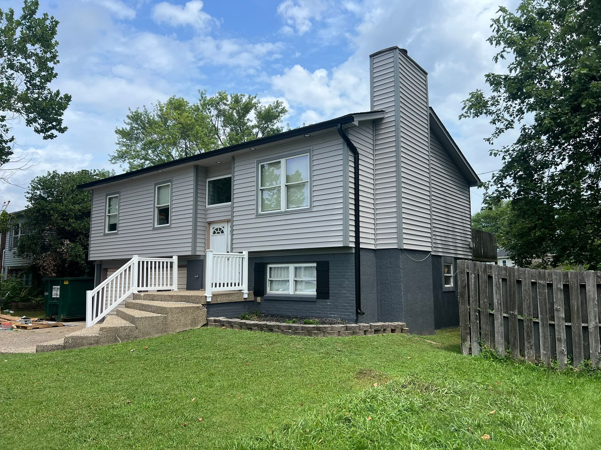 Two-story gray house with white trim, black shutters, chimney, and wooden fence.