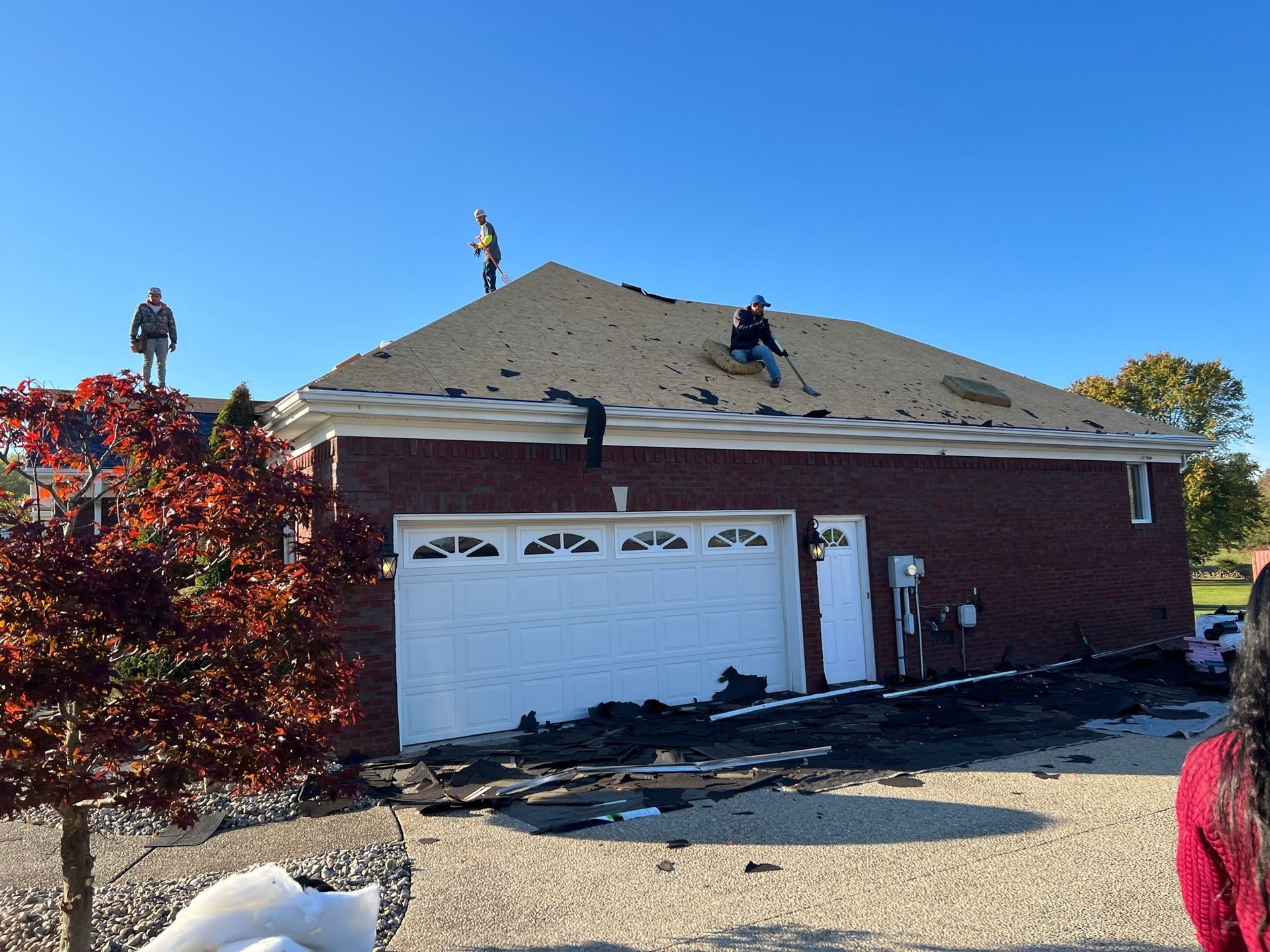 Roofers working on a brick house with a white garage door under a blue sky.