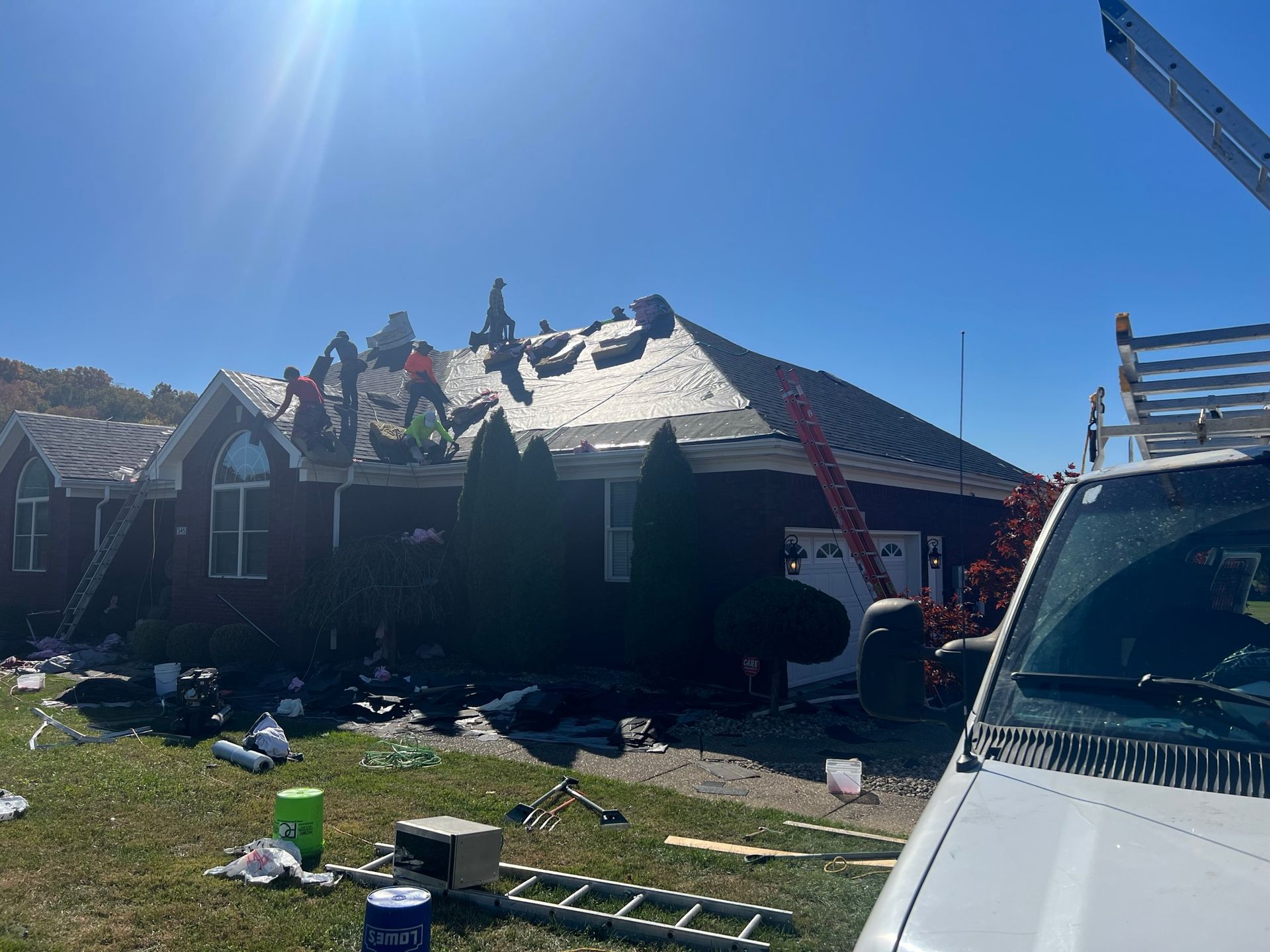 Roofing crew working on a house. Blue sky, ladders, and equipment visible.