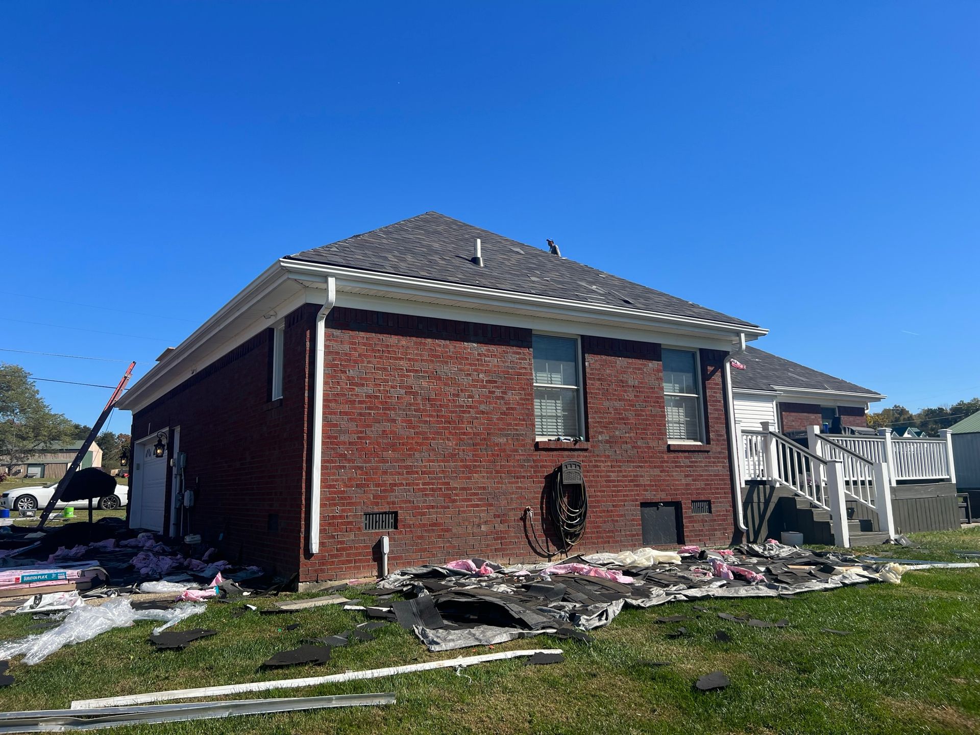 Red brick house with debris on the ground, white trim, dark roof, clear blue sky.