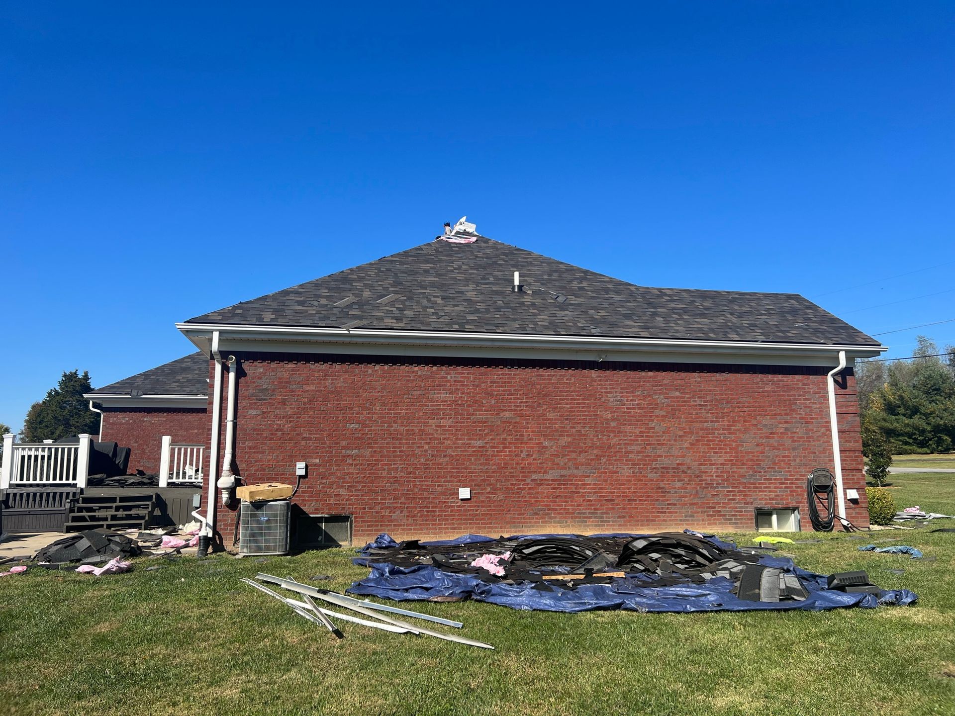 Red brick house with a gray roof against a clear blue sky. Debris and equipment on the lawn.