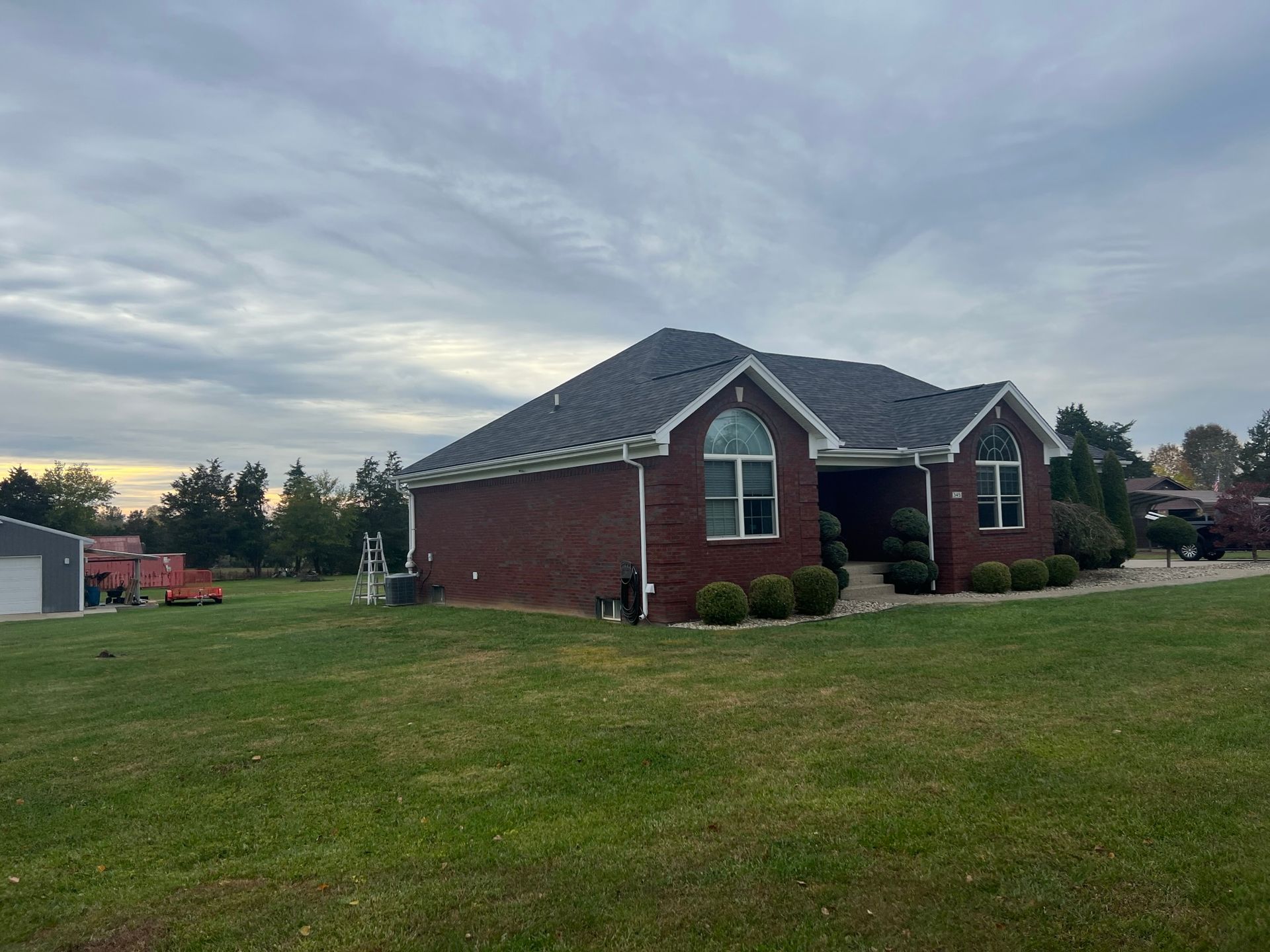 Red brick house with a dark roof, a large front yard, and a cloudy sky.
