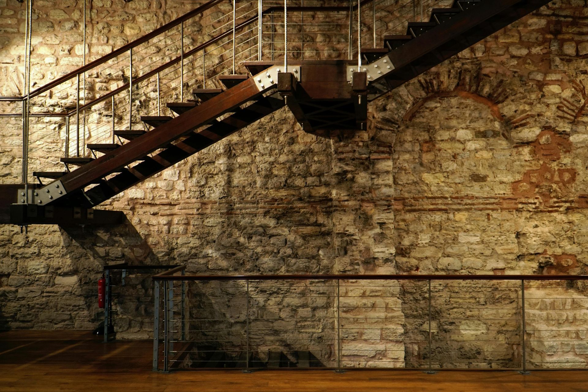 Staircase with wooden steps and metal railing against an old stone wall.
