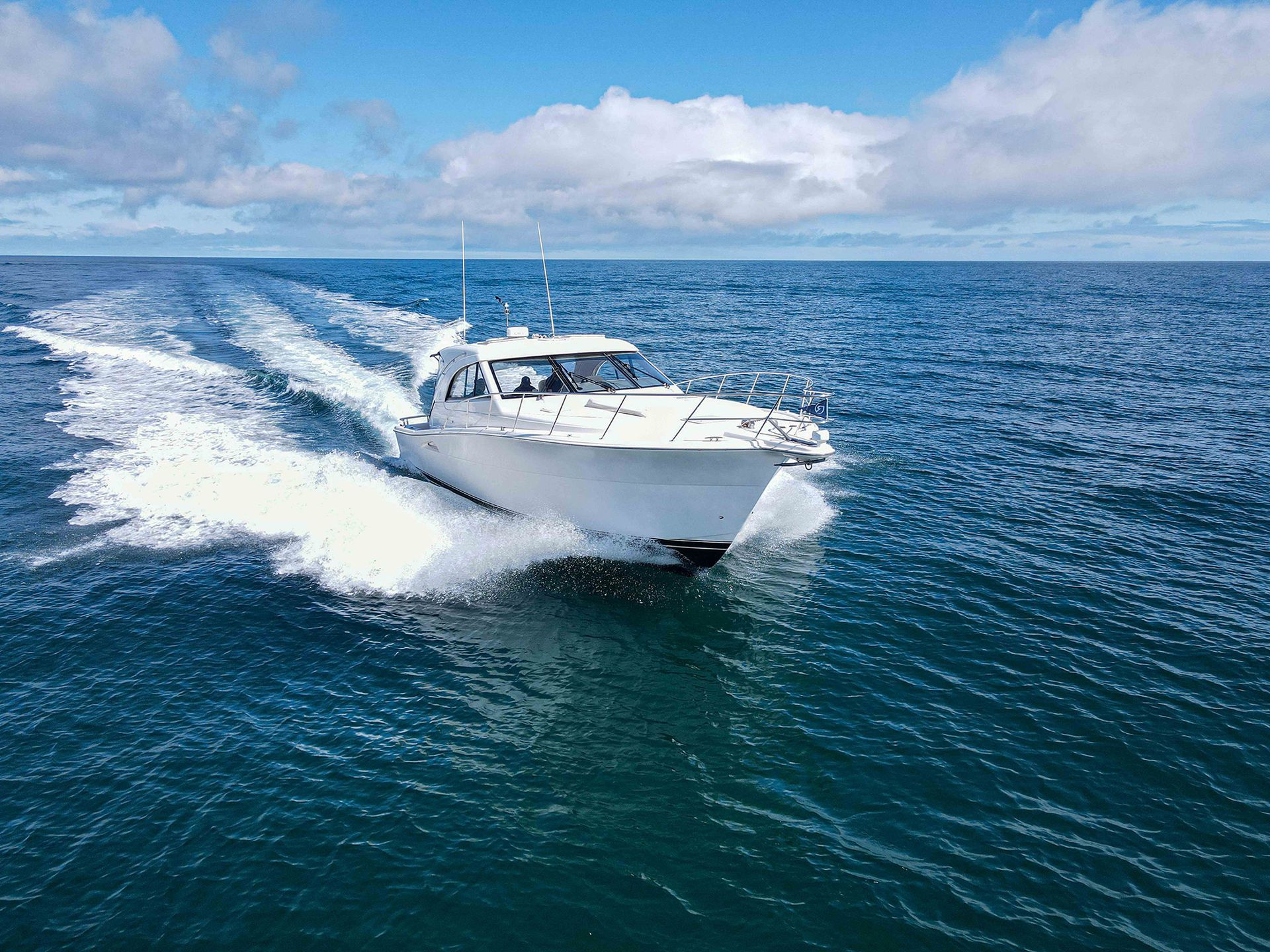 White motorboat speeding across blue ocean, creating a white wake under a partly cloudy sky.
