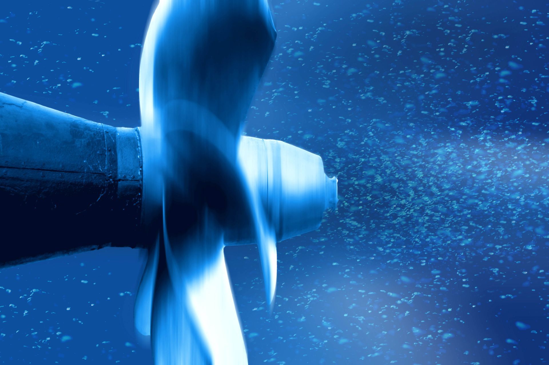 Blue-toned photo of a boat propeller underwater, churning bubbles.