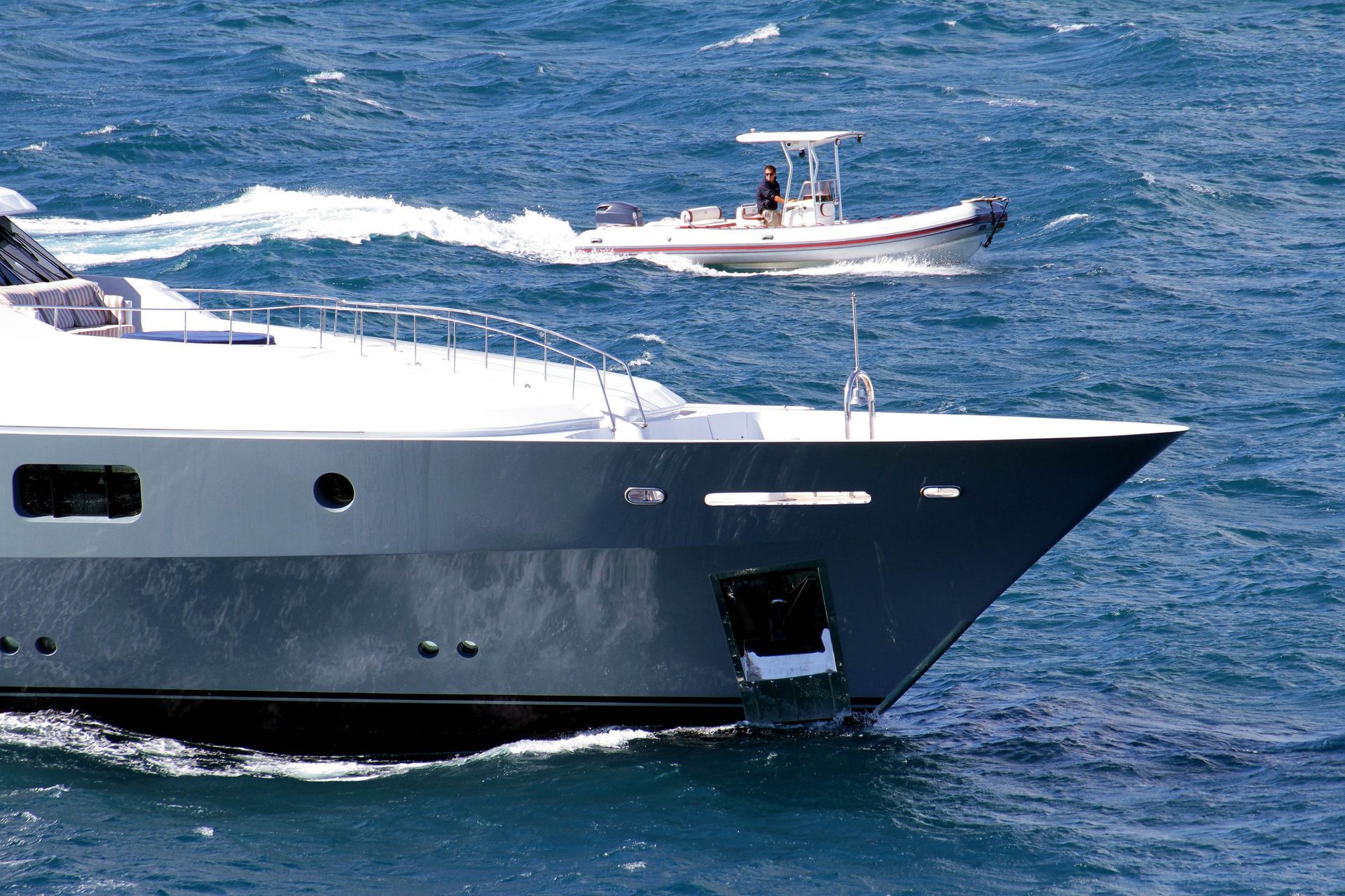 Large gray yacht in ocean, small white boat behind it.