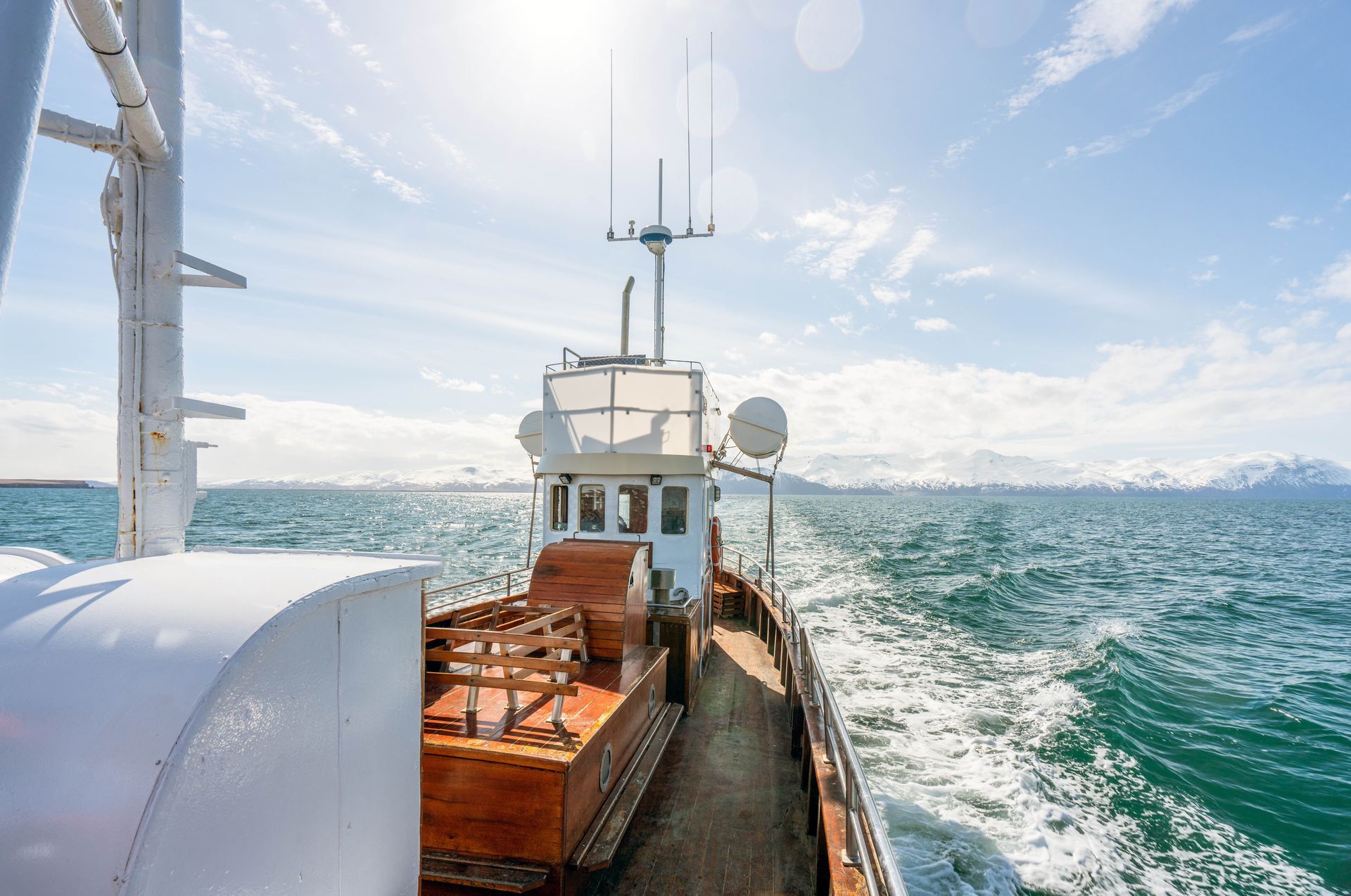 Boat sailing on a blue sea under a sunny sky, mountains in the distance.