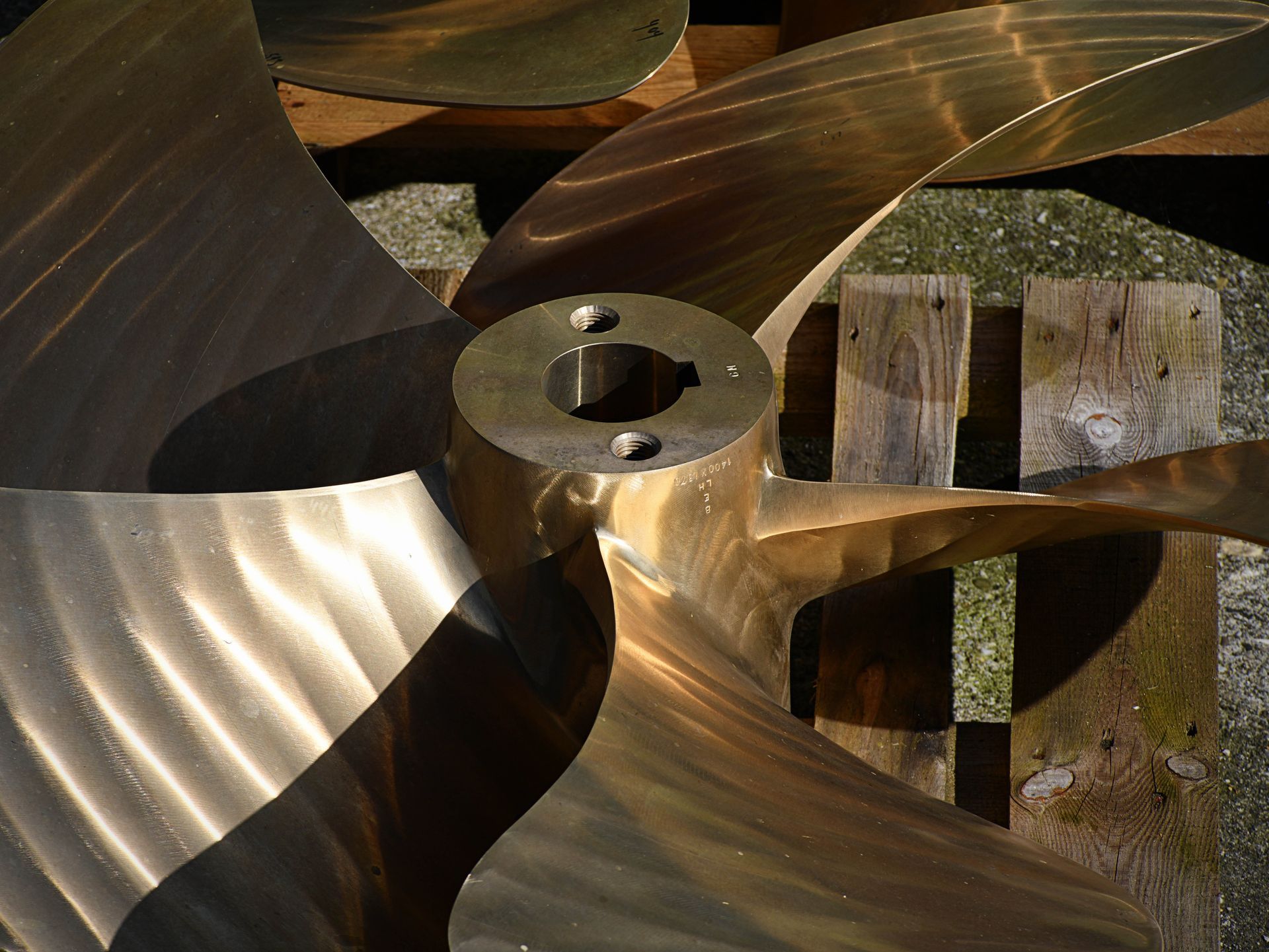 Close-up of a bronze boat propeller resting on a wooden pallet, blades in full view.