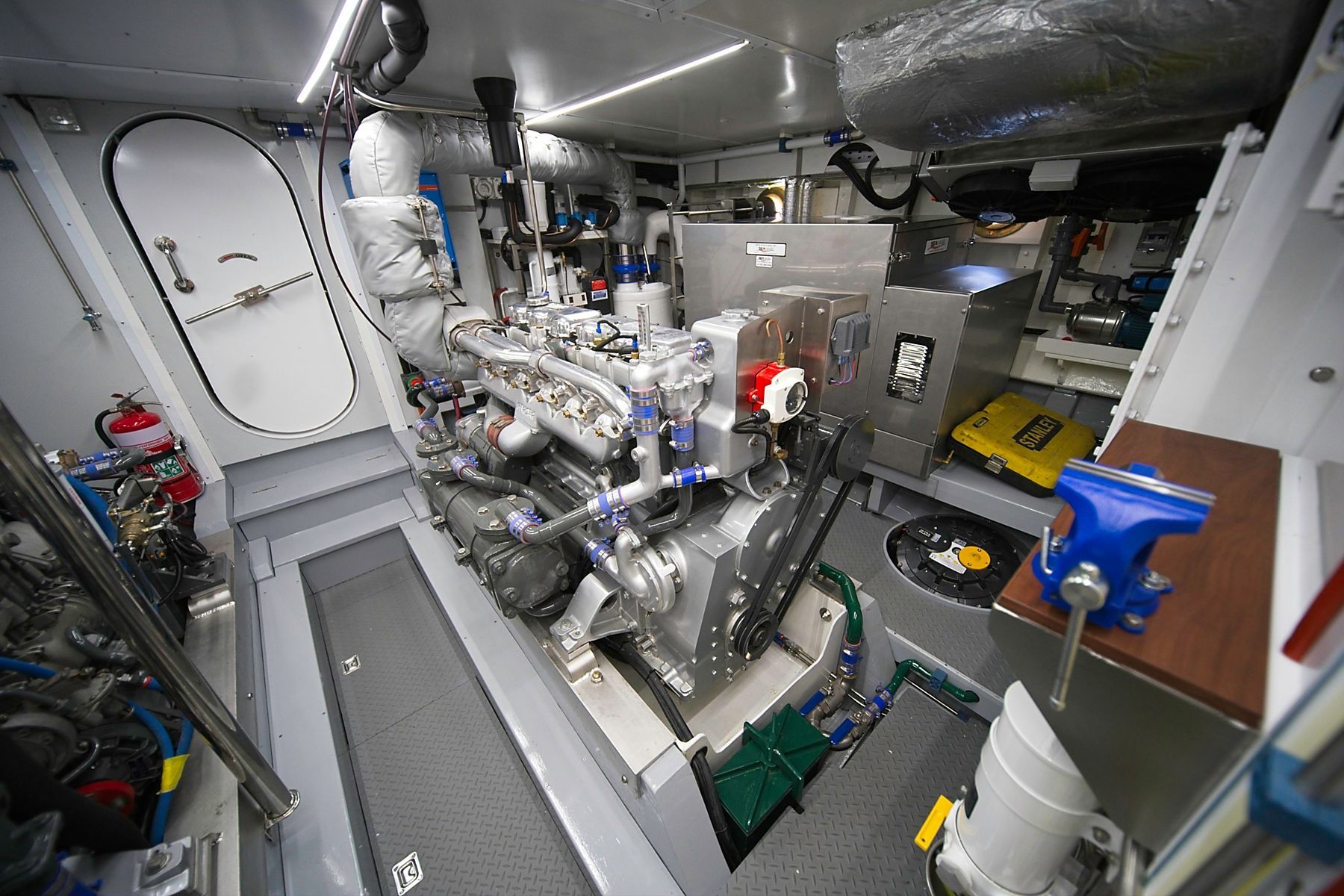 Hydraulic control panel with silver pipes and black hoses, mounted on a wall with ropes.