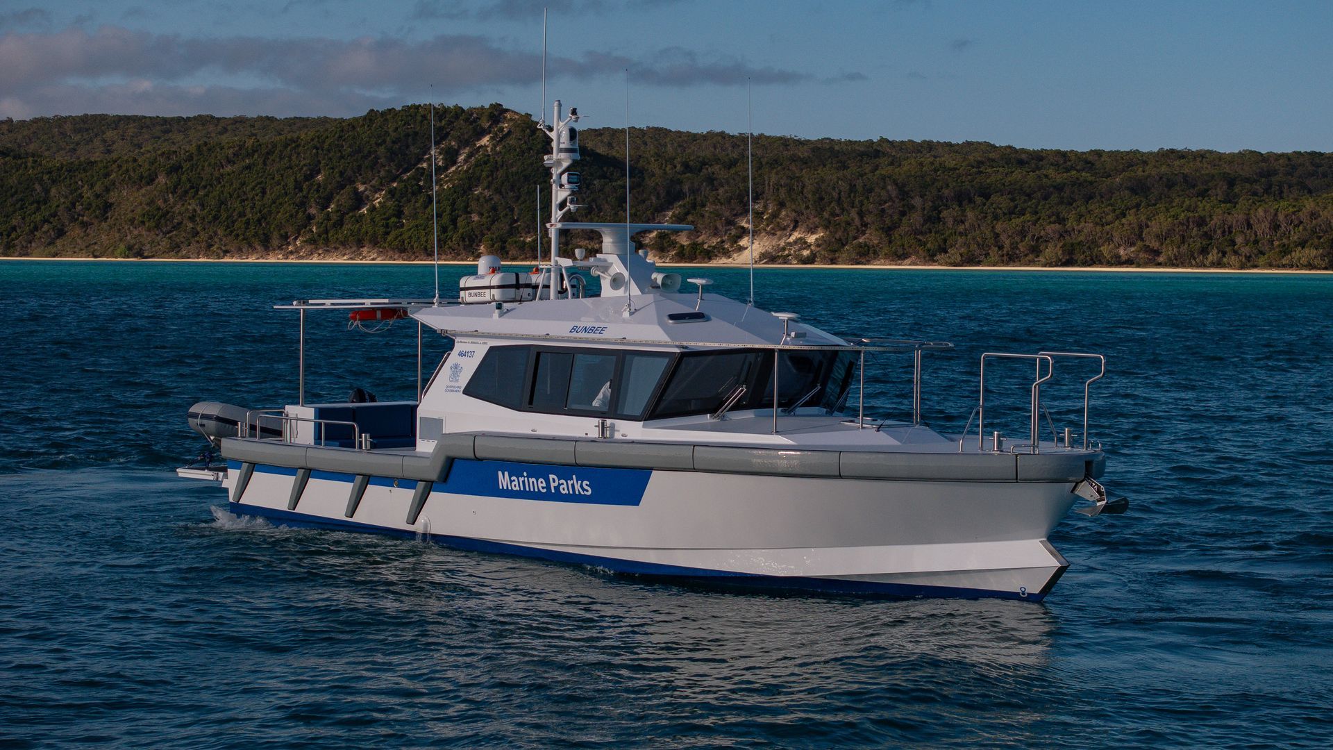 Fishing boat traveling on blue water, under a cloudy sky near a hilly coast.