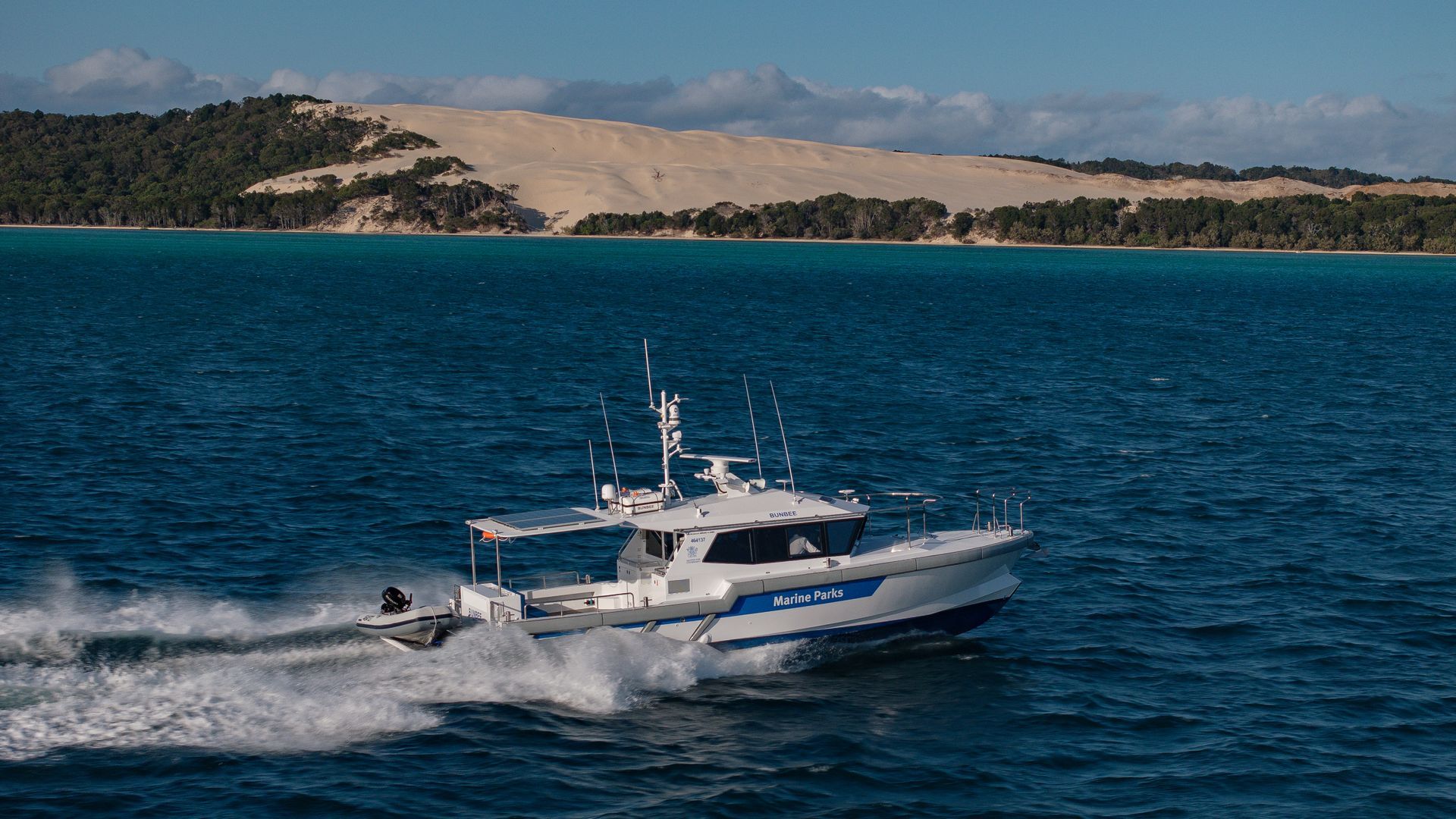 Orange fishing boat docked at a pier, blue water and sky in the background.