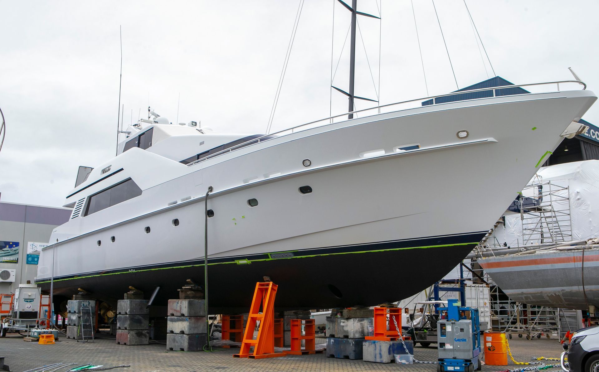 White yacht in dry dock, supported by blocks and jacks. Hull is black and green.