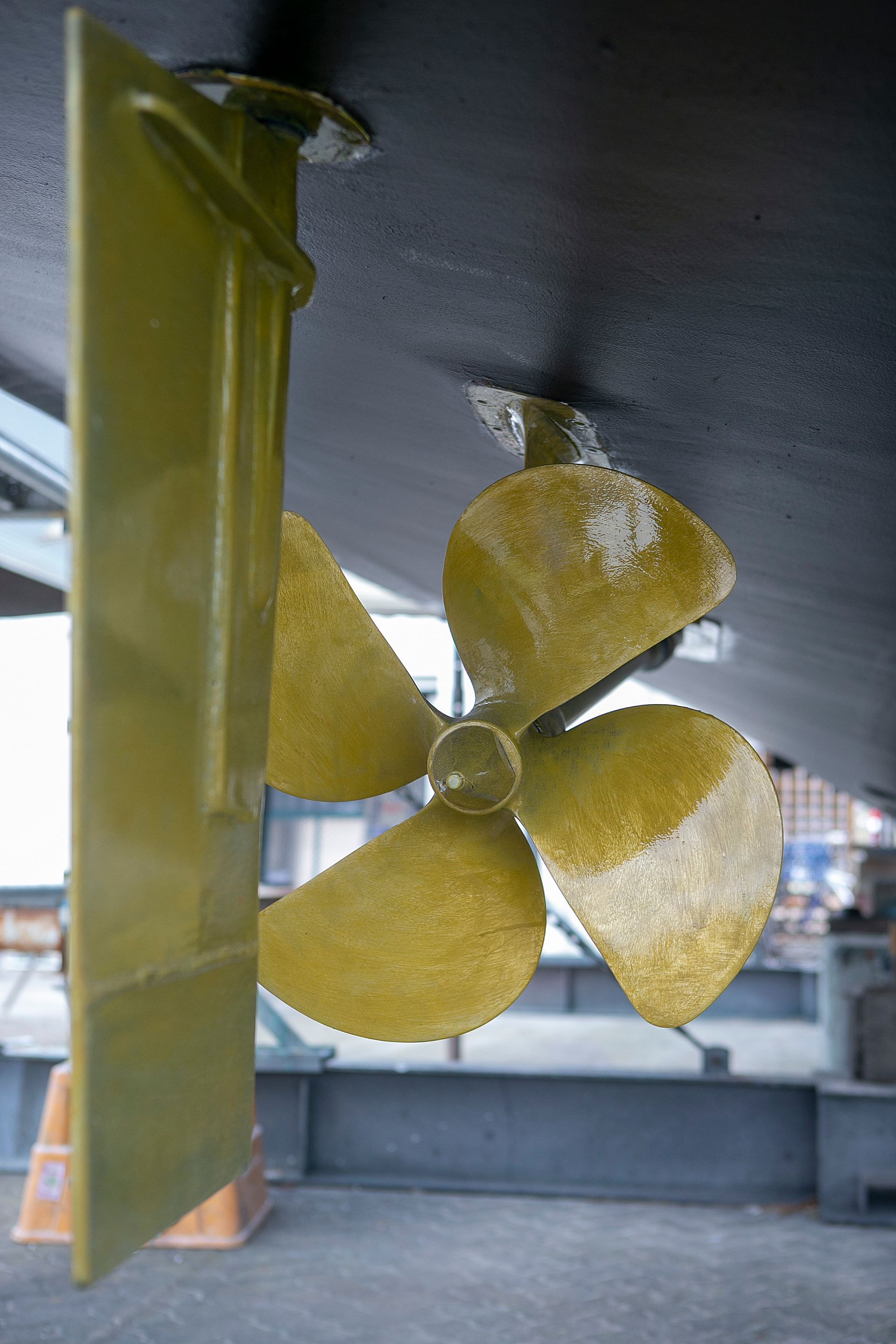 Person holding boat propeller, possibly for maintenance, near a boat hull.
