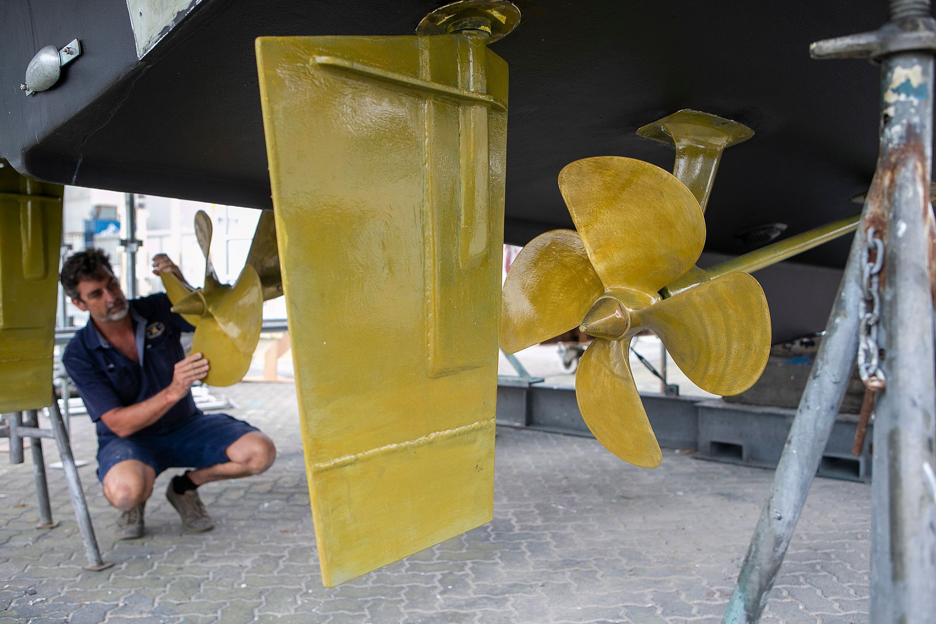 Bronze boat propeller, mounted on dark gray hull, against a light gray surface.