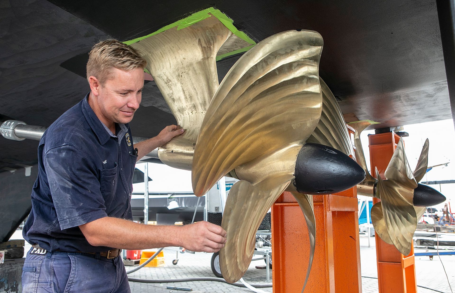 Two bronze ship propellers, mounted on a light blue hull, supported by wooden blocks.