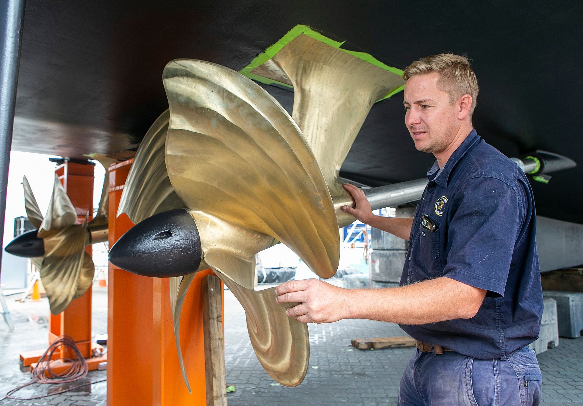 Man working on a boat propeller, with a bright orange support structure.