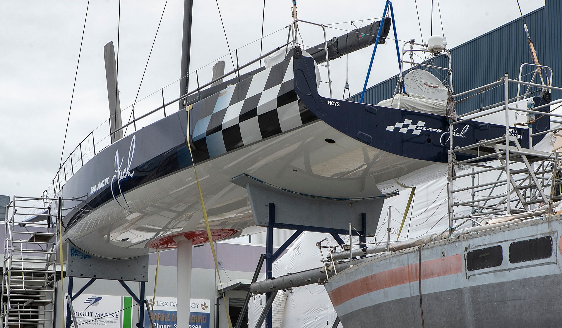 Sailboat suspended in a shipyard, white hull, black and white checkered pattern on the stern.