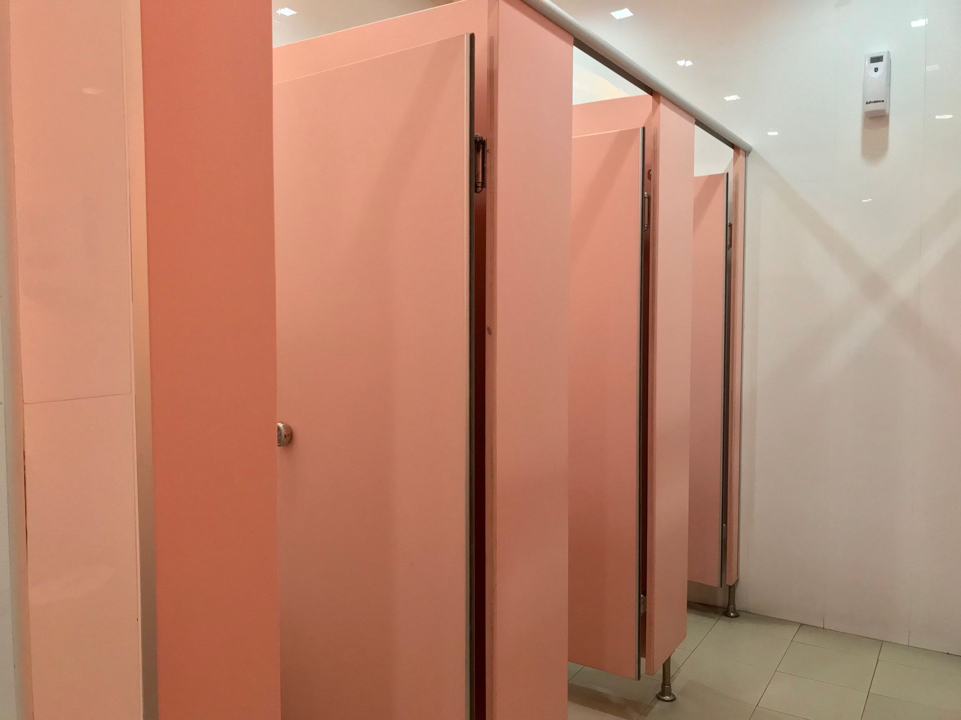 A row of pink toilet cubicles in a public restroom.
