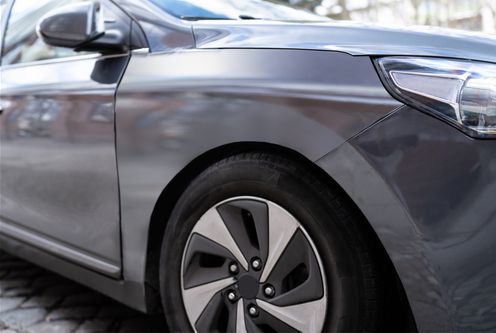 Close-up view of the front fender and wheel of a gray car parked on a cobblestone surface.