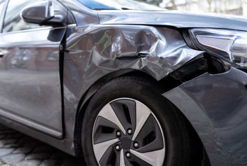 A close-up view of a gray car's front fender showing significant denting and bodywork damage.
