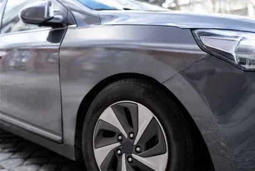 Close-up view of the front fender and wheel of a gray car parked on a cobblestone surface.