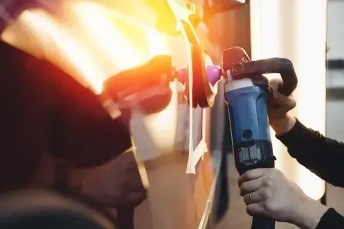 A person uses a rotary buffer to polish the side of a vehicle in a garage.