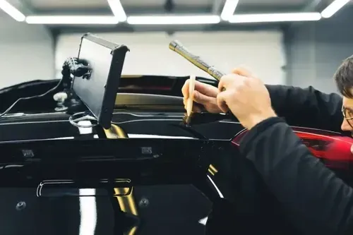 A technician uses a specialized light and tool to perform paintless dent repair on the glossy black body of a vehicle.