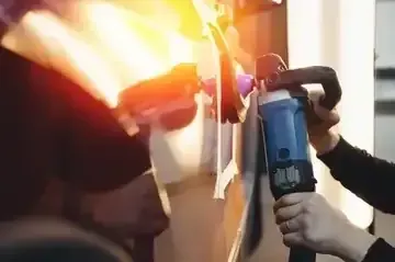 A person uses a rotary buffer to polish the side of a vehicle in a garage.
