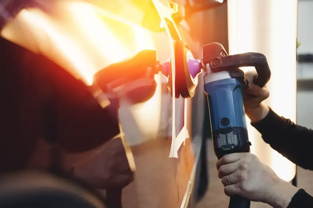 A person uses a rotary buffer to polish the side of a vehicle in a garage.