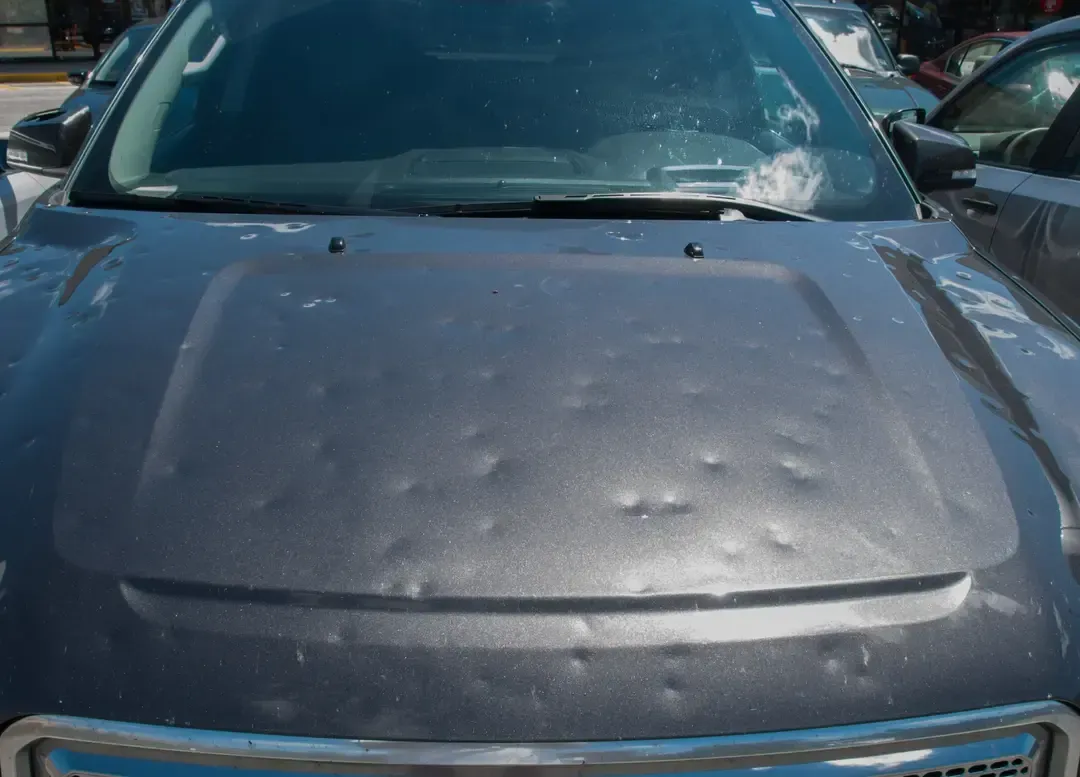 Close-up of a dark grey car hood covered in numerous dents caused by hail damage.