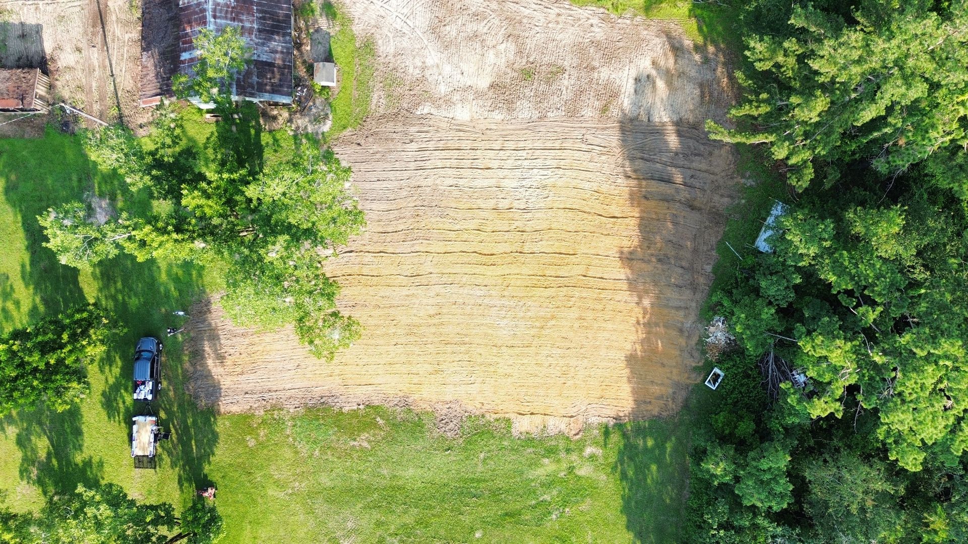 Aerial view of a large stone wall beside trees and grass, with a parked scooter at the bottom left.