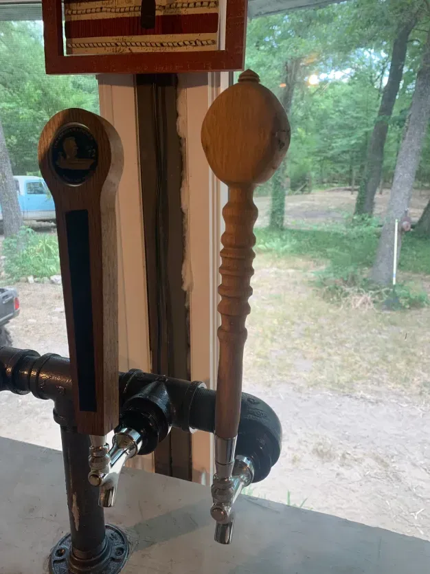 Three wooden beer taps are sitting on a table in front of a window.