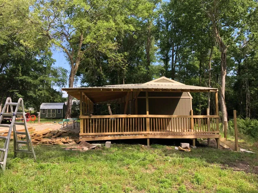 A small house with a porch is being built in the middle of a grassy field.